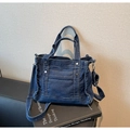 Donkerblauwe denim crossbody handtas met zilveren noppen en mini-bedeltas op een boek - Donkerblauw