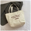 Detailansicht der cremeweißen Canvas-Tragetasche mit braunem Vintage-Buchstabendruck - Vertikales Weiß
