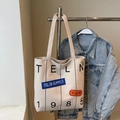 Detailed view of canvas tote bag featuring premium embroidery patches and printed letters - Khaki