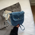 Detail of a mini washed denim crossbody bag with silver button snap closure and textured fabric - Light Blue