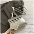 Silberne Handtasche mit Knitteroptik und Herzanhänger auf grauem Anzug präsentiert - Silber