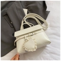 Detail der cremeweißen PU-Ledertasche mit Spitzen-Herz-Anhänger auf grauem Blazer-Hintergrund - Weiß