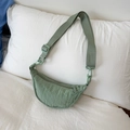 Detalle de bolso medialuna de nailon verde salvia con correa ajustable sobre cama blanca - Verde Menta