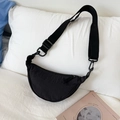 Detalle de bolso medialuna de nailon negro con correa ajustable sobre fondo de ropa de cama - Negro