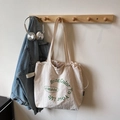 Beige canvas tote bag with green letter print and drawstring closure in minimalist style - Off White