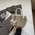 Chic beige tote bucket bag with dog pendant and detachable shoulder strap in hand - White
