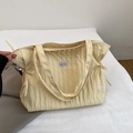 Detalle del bolso tote acolchado amarillo claro con textura plisada y etiqueta de marca - Amarillo