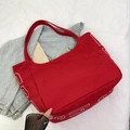 Red canvas tote bag with bold white lettering on casual denim jacket background - Red