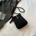 Detalle de bolso bandolera de nailon negro con cordón y hebilla sobre un fondo blanco - Negro