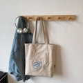 Beige Canvas-Tragetasche mit zwei Fronttaschen und blauer Stickerei in Lifestyle-Umgebung - Cremeweiß