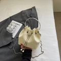 Detail of cream bucket bag showing silver round handle, butterfly buckle and pearl charms - Yellow