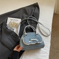Detailed close-up of blue denim bow handbag with lace trim on a grey suit background - Blue and Silver