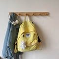 Detail eines hellgelben Rucksacks mit weißem Bärenanhänger und Logo-Etikett vorne - Mit Anhänger / Gelb