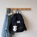 Detail eines minimalistischen schwarzen Nylon-Rucksacks mit weißem Plüschbären-Anhänger - Mit Anhänger / Schwarz