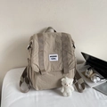 Detail of khaki nylon backpack featuring a plush bear charm and laptop desk setting - With Charm / Khaki