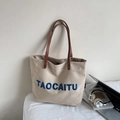 Detail of beige canvas tote with blue embroidery and brown leather handles and rivets - Beige Grey