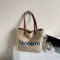 Detail of canvas tote bag featuring blue TAOCAITU embroidery and brown leather handles - Khaki