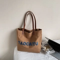 Detail of canvas tote bag with blue embroidered letters and premium brown leather straps - Caramel color
