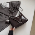 Detail van donkerbruine lederen okseltas met zilveren ketting en mini tasje op een pak - Koffie groot