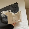 Bolso de hombro blanco crema con textura vertical y lazo en un entorno elegante - Blanco Roto