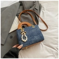 Detail of blue denim shoulder bag featuring brown leather strap and pearl bow charm - Royal Blue With Pendant