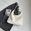 Detailaufnahme der cremefarbenen Hobo-Tasche aus Leder auf grauem Blazer mit Deko - Cremeweiß