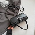 Detail view of black matte leather baguette bag with silver metallic clasp on grey suit - Black