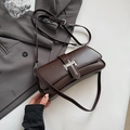Detail of dark brown glossy leather baguette bag with silver metal buckle on a blazer - Brown