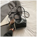 Macro shot of black glossy handbag with round handle and tassel on grey blazer - Black With Pendant