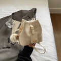 Chic beige checkered bucket bag with gold hardware and plush charm on white bed - Cream White With Pendant