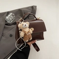 Detail der dunkelbraunen glänzenden Handtasche mit goldenem Drehverschluss und Plüschbär-Anhänger - Kaffee Mit Anhänger