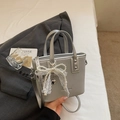 Detalle de bolso saco plateado con lazo de encaje de perlas y asas metálicas - Plata con colgante