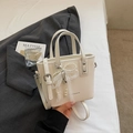 Detalle del bolso tipo cubo crema con colgante de lazo de perlas y encaje y correa - Blanco Roto Con Colgante
