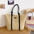 Detail der beigen Strohtasche mit Wabenmuster und schwarzen Seilgriffen auf Holztisch - Beige & Schwarz