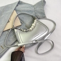Detalle de bolso media luna plateado con asa de perlas y correa ajustable sobre denim - Plateado