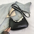 Close-up of black crescent shoulder bag with pearl heart chain on denim background - Black