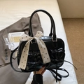 Polished black Boston bag with ribbon details and a polka dot scarf on a bed - Black