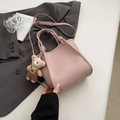 Detail view of pink lychee textured leather handbag with plush bear charm and metal feet - Pink With Pendant