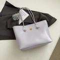 Detail der fliederfarbenen Lackleder-Tote-Bag mit goldenem Logo auf grauem Anzug - Lila