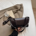 Borsa baguette vintage marrone scuro con catena d'argento e tracolla su letto bianco - Marrone