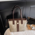 Close-up of canvas tote bag with brown leather handles and golden metal buckle detail - Gray