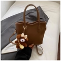 Close-up of brown pebbled leather handbag with brand embossing and a plush bear charm - With Charm / Brown