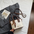 Vue de dessus d'un sac seau crème avec bordure brune et breloque perlée sur blazer gris - Blanc Cassé (Avec Pendentif) / Blanc Crème avec Pendentif