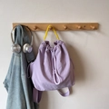 Mochila de cordón lila con asa amarilla en contraste colgada en un perchero de madera - Morado