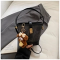 Detail of black bucket bag with gold clasp and cute plush bear charm on a suit fabric - Black with Pendant