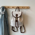 Eleganter cremeweißer Mattrucksack mit braunen Lederriemen an einem Holzhaken hängend - Gebrochenes Weiß