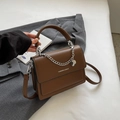 Detail einer braunen eckigen Ledertasche mit Silberkette und Metall-Markenanhänger - Braun