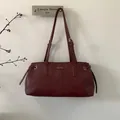 Detailansicht der weinroten Ledertasche mit verstellbaren Trägern und Metall-Markenlogo - Burgunderrot