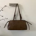 Vista macro de bolso bandolera de cuero marrón retro con hebillas plateadas y logo metálico - Marrón