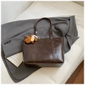 Detail of deep brown tote bag with bear charm on a grey suit jacket background - Coffee With Pendant